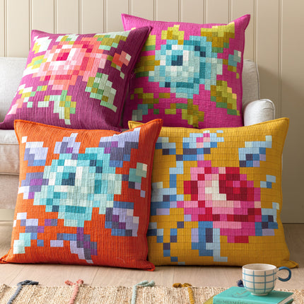 Colorful pixelated cushions on a sofa with a cup and books in the background.