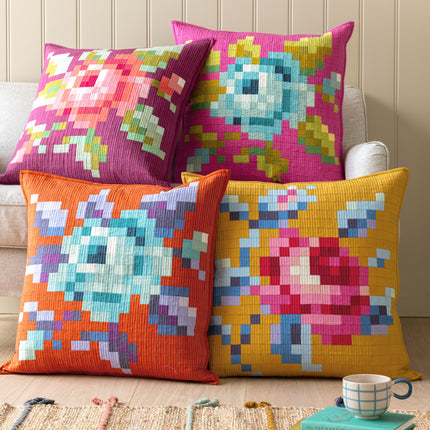 Colorful pixelated cushions on a sofa with a cup and books in the background.