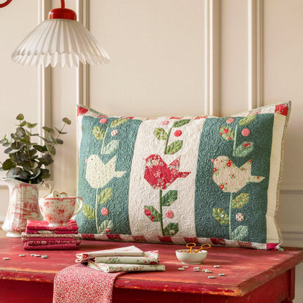 Decorative pillow with bird pattern on a red table against a neutral wall.