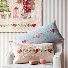 Decorative pillows with floral and heart patterns on a chair, with a Christmas-themed wall hanging in the background.